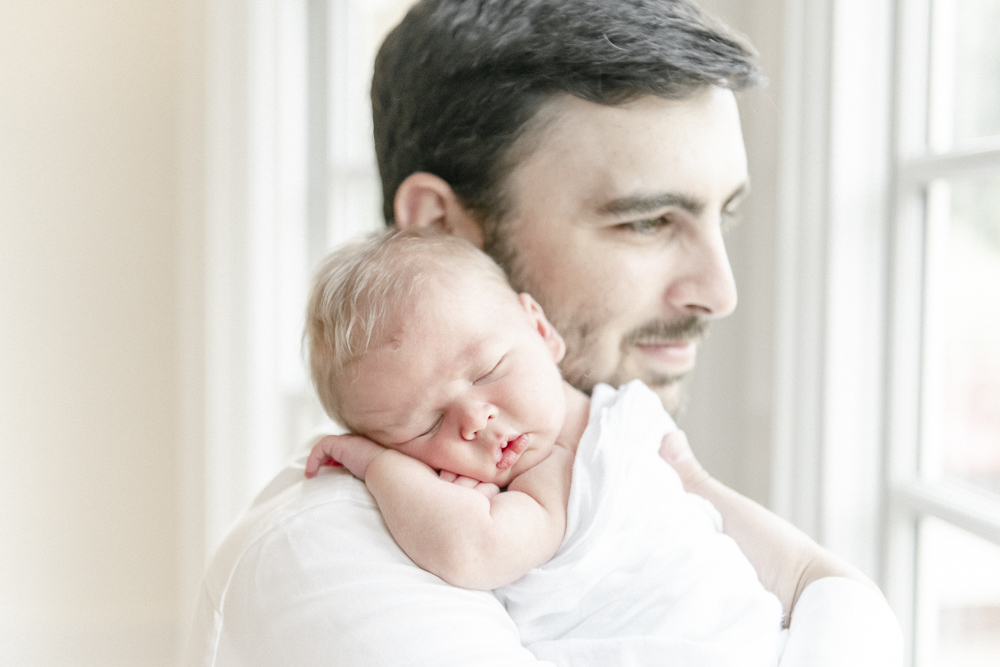 A newborn baby sleeps on his father's shoulder