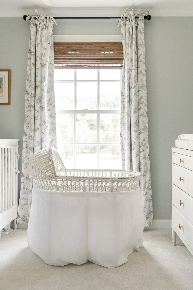 A white Pottery barn bassinet sits in front of a bright window