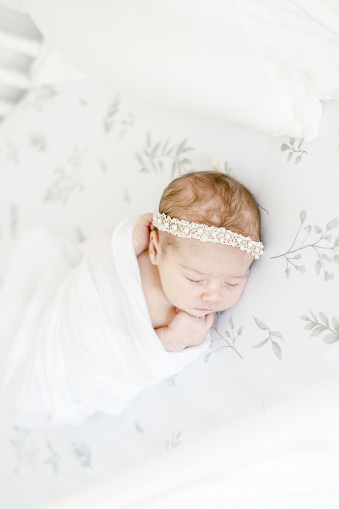 Newborn baby girl wears a lacy and pearl headband swaddled in white