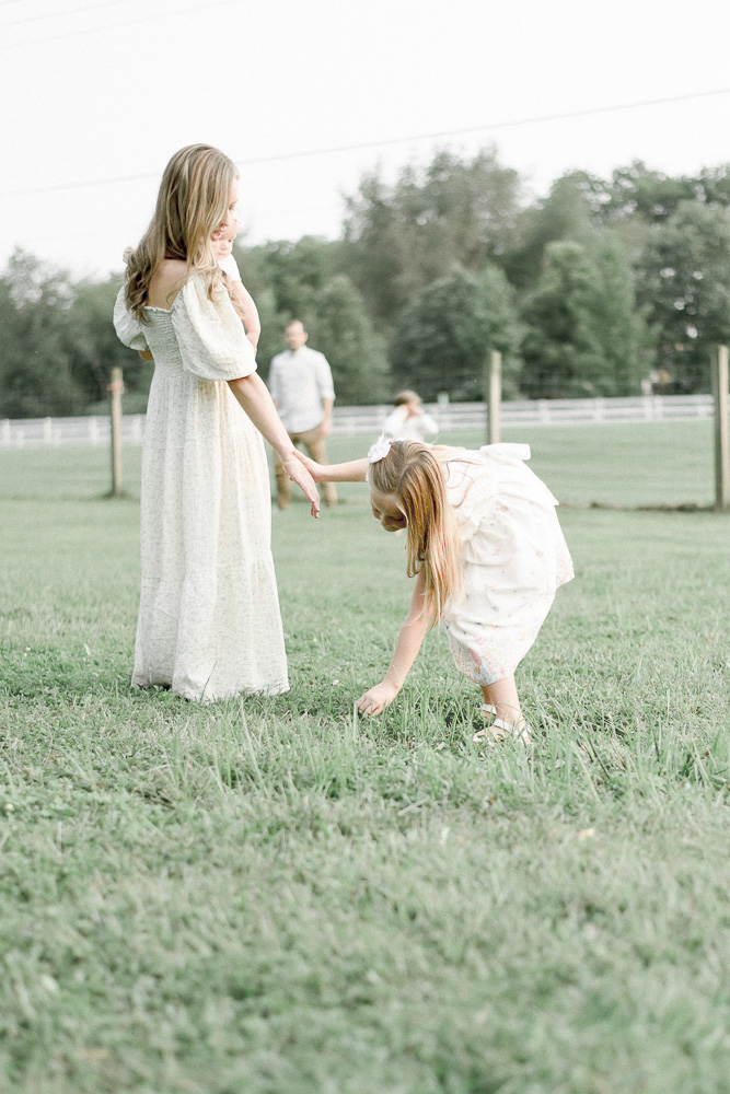 A young girl picks a dandelion while holding her mother's hand