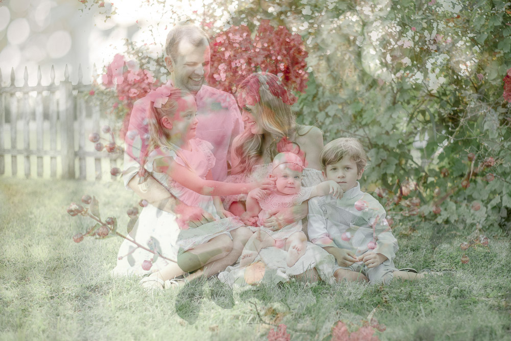 Double exposure of pink flowers on top of a family of 5 near a white picket fence.