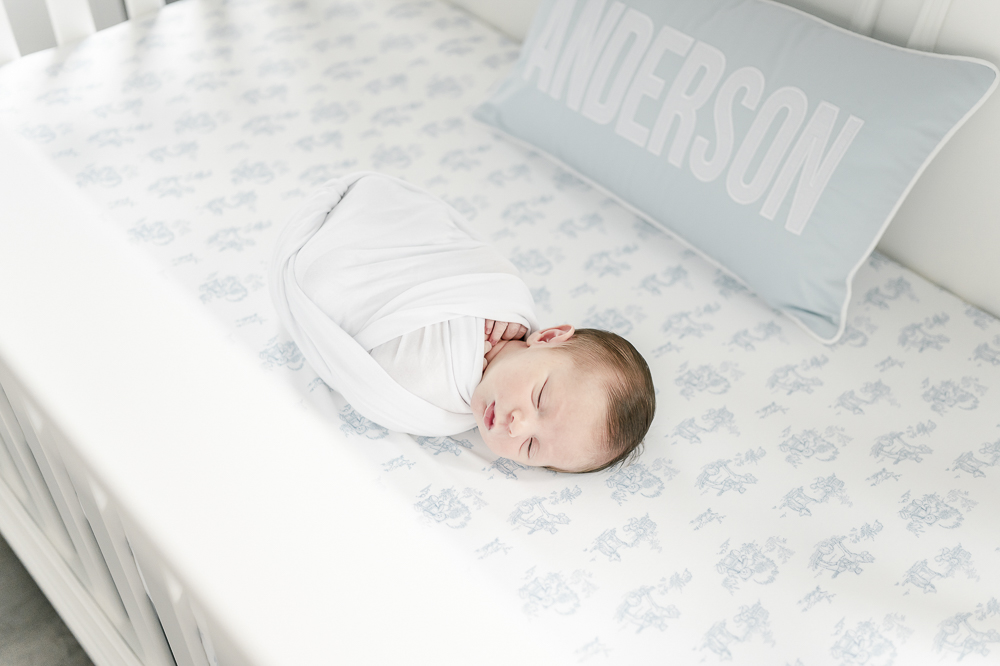 Newborn boy sleeps in his crib with a pillow monogrammed with the name Anderson