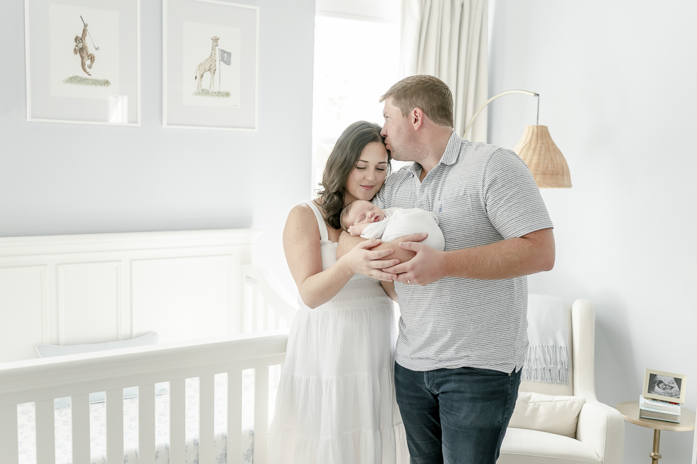 A husband holds his baby boy and kisses his wife by the best nashville newborn photographer Kristie Lloyd