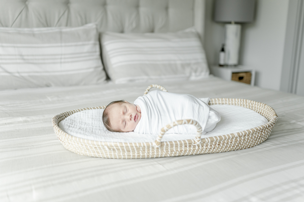 A newborn sleeps in a Moses basket sitting on a master bed by the best nashville newborn photographer Kristie Lloyd
