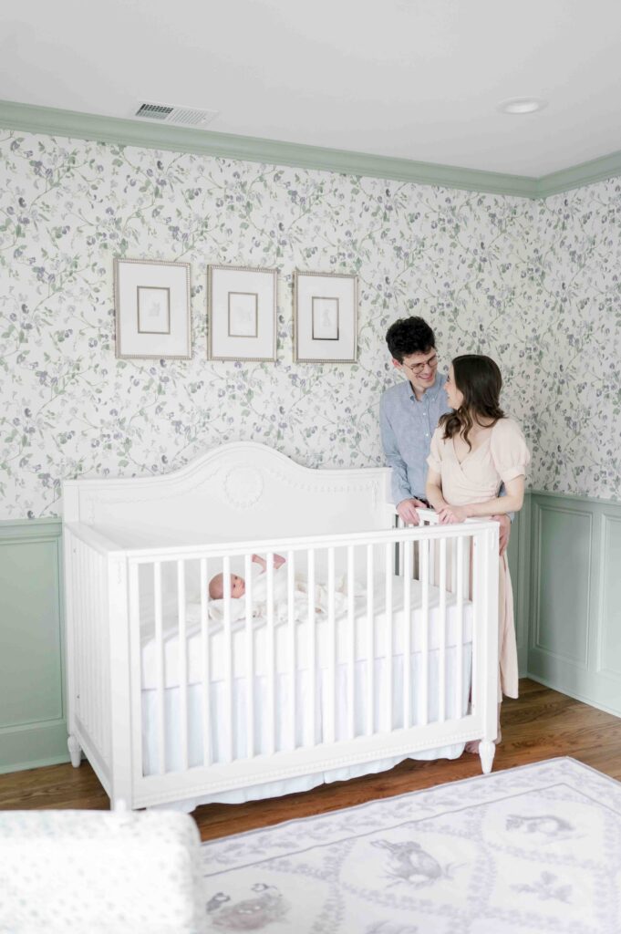 New parents smile at each other standing over their newborn's crib during their Nashville in-home newborn session