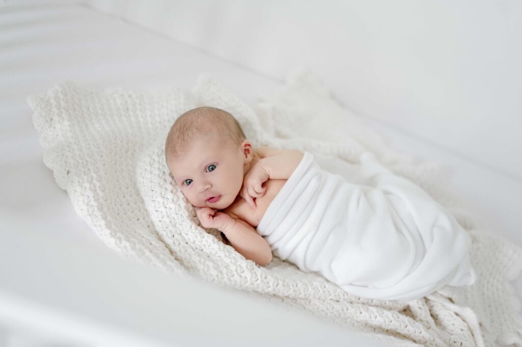 a newborn girl lays on a white blanket in her crib
