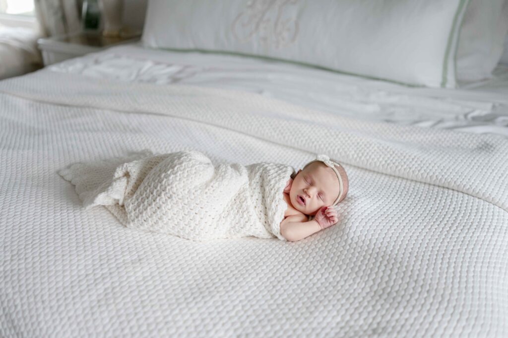 newborn baby wrapped in a white swaddle sleeps on a master bed