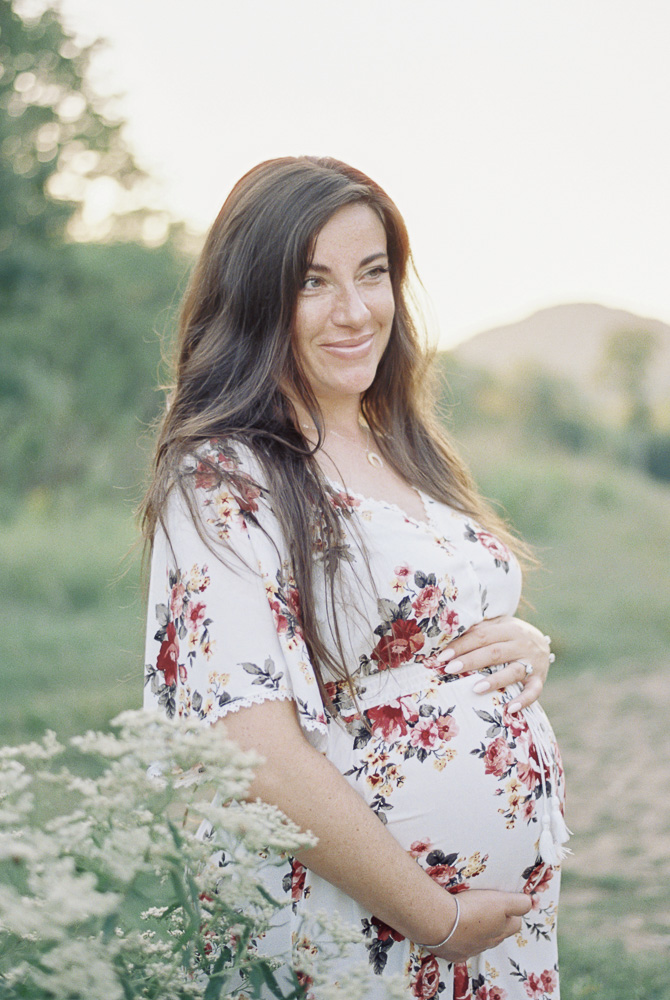 A woman smiles off in the distance as she holds her pregnant stomach.
