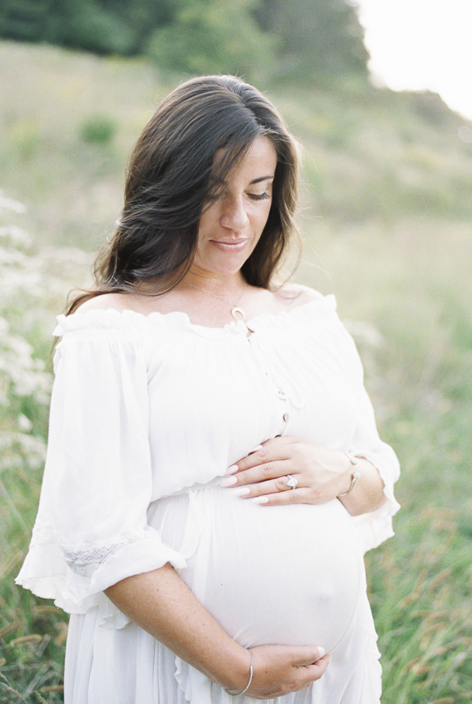 A brunette woman smiles down at her pregnant stomach