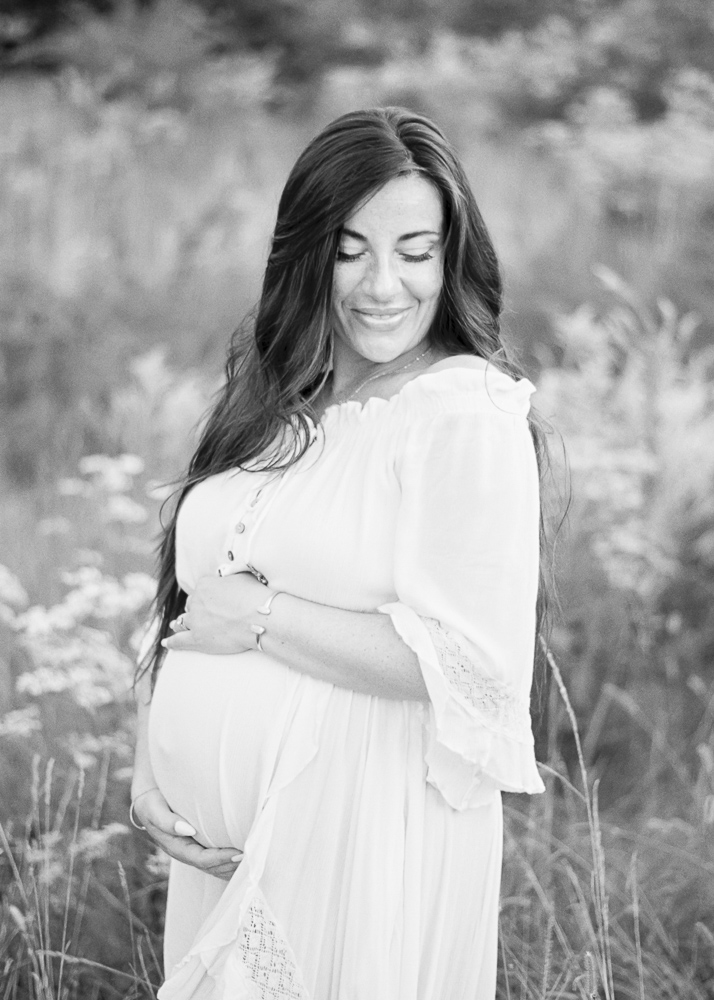 Black and white image of a pregnant woman in a white dress smiling over her shoulder