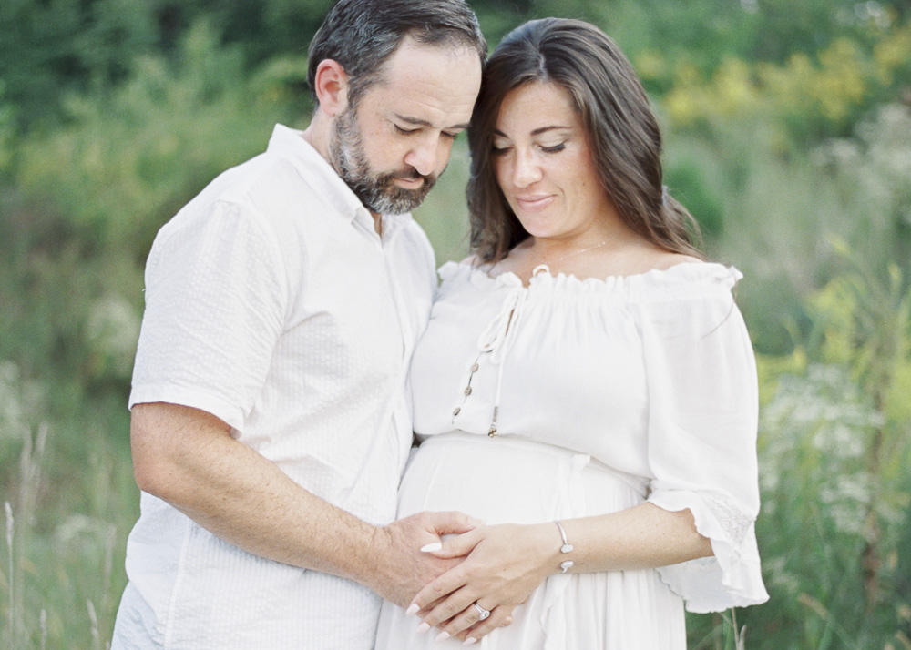 A man and woman embrace her pregnant stomach and smile