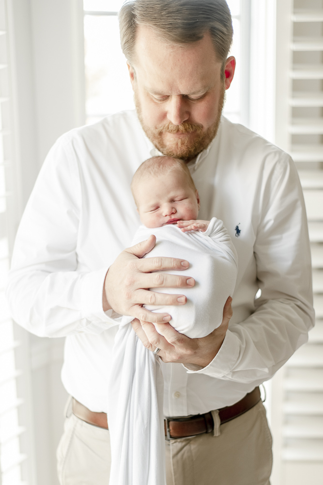 A dad holds his newborn son swaddled in white