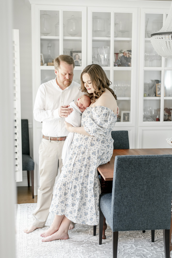 New parents hold their newborn standing in a dining room