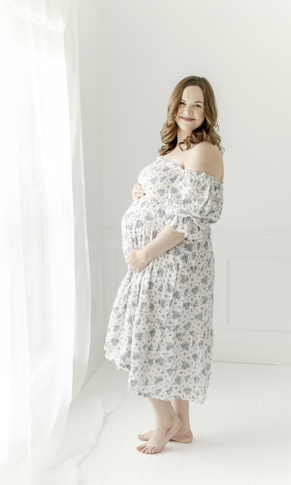 Pregnant woman smiles as she stands in a blue floral dress 