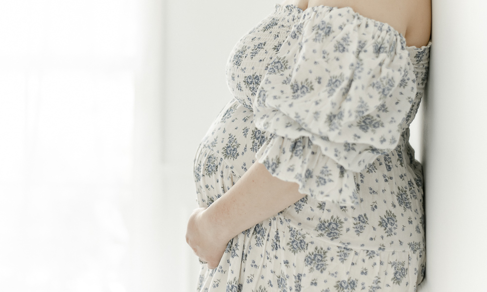 Pregnant woman holds her stomach wearing a blue floral dress