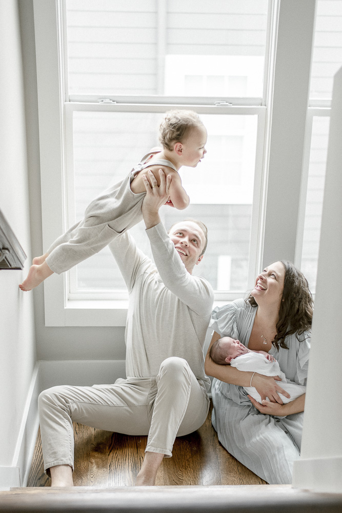 A father holds his toddler in the air during a lifestyle newborn photographer session