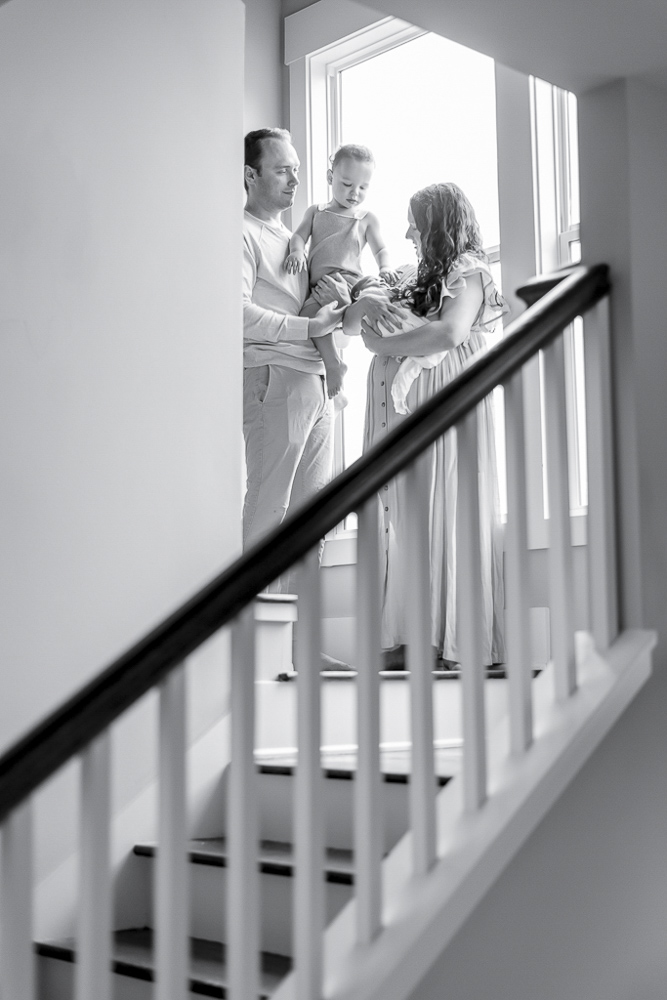 Black and white image of a family standing at the top of a stairwell with a newborn and a toddler