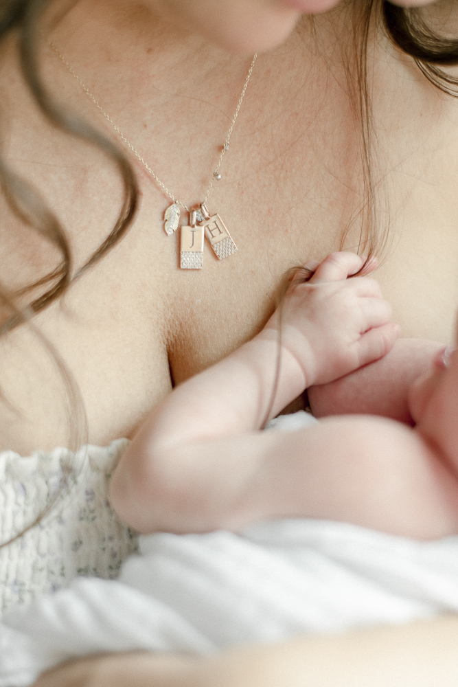 Infant fingers are tangled in her mother's hair next to a monogrammed necklace