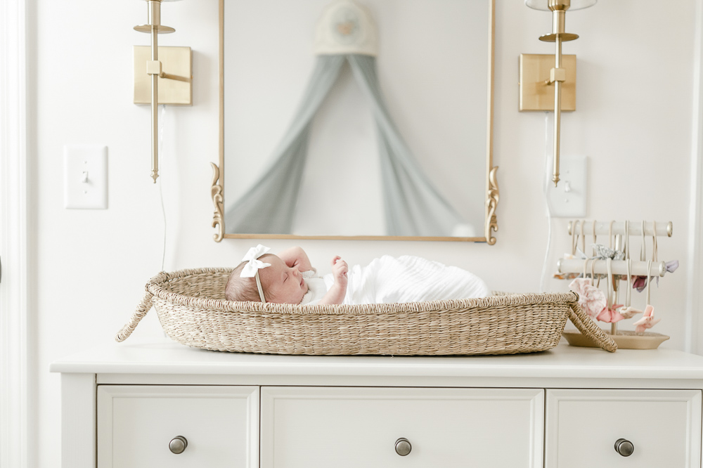 A newborn baby wearing a white bow sleeps in a moses basket