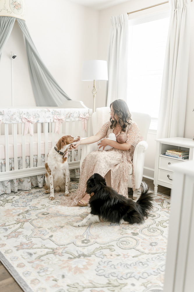 A mother pets her dog while holding her newborn in the whimsical nursery