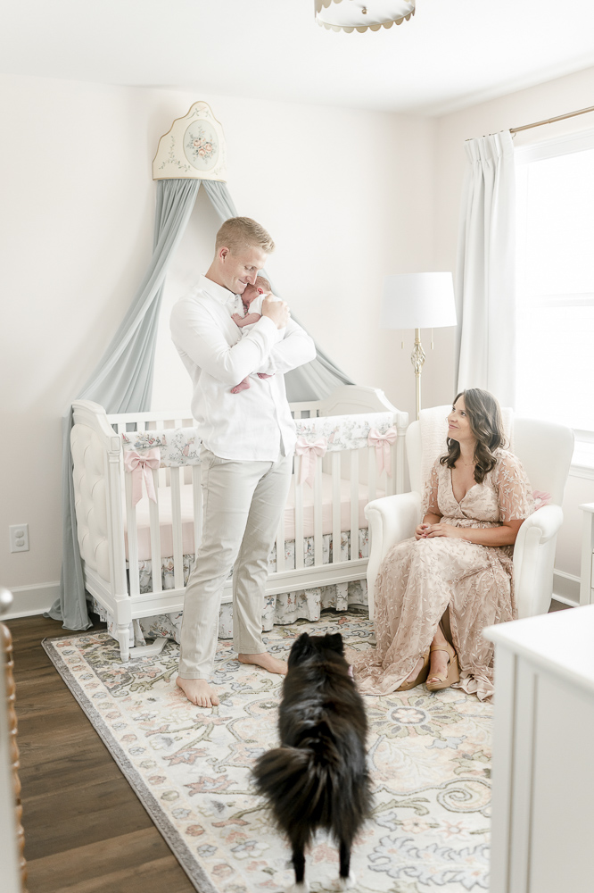 A father cuddles his newborn as his wife smiles up at him from the rocking chair by newborn photographer Kristie Lloyd