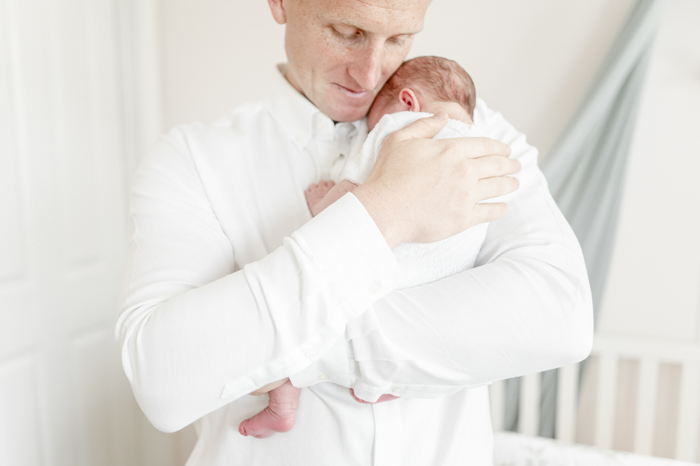A fathers arms embrace his newborn by newborn photographer Kristie Lloyd