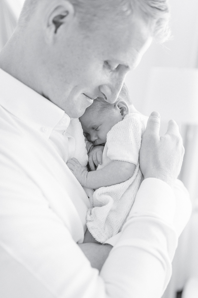 Black and white image of a newborn curled asleep in her fathers arms