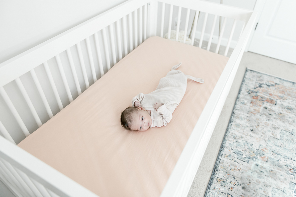 Newborn baby laying on a pink sheet in a white crib