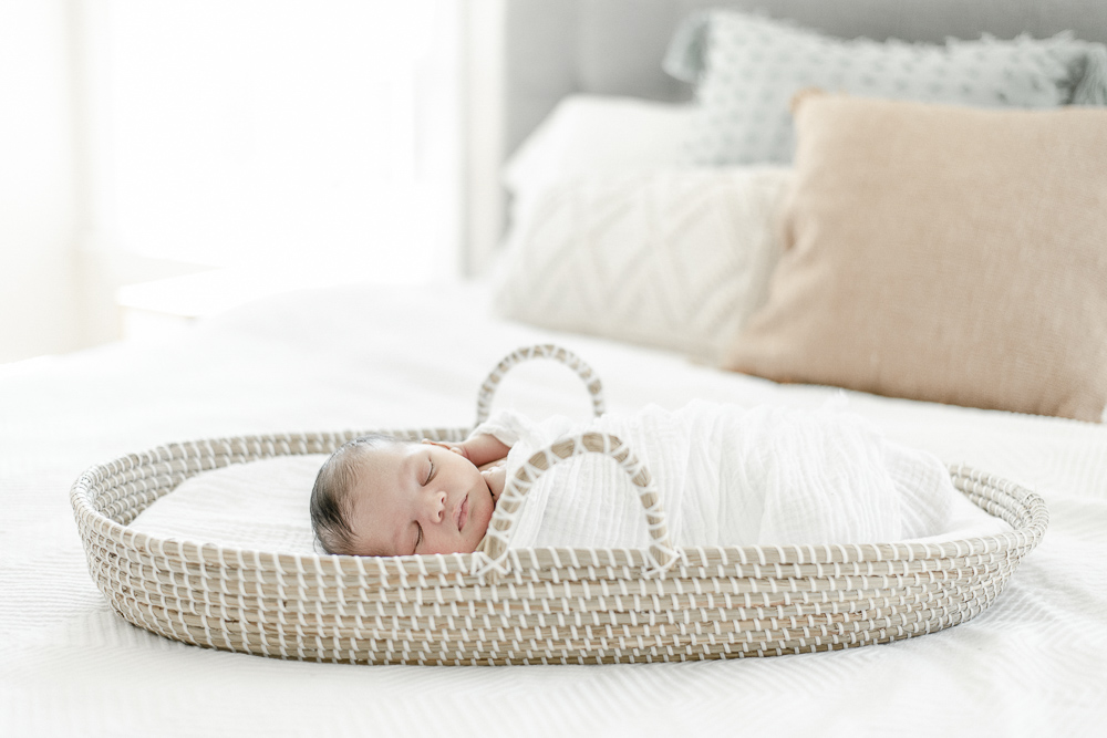 A newborn baby sleeps in a moses basket on the master bed