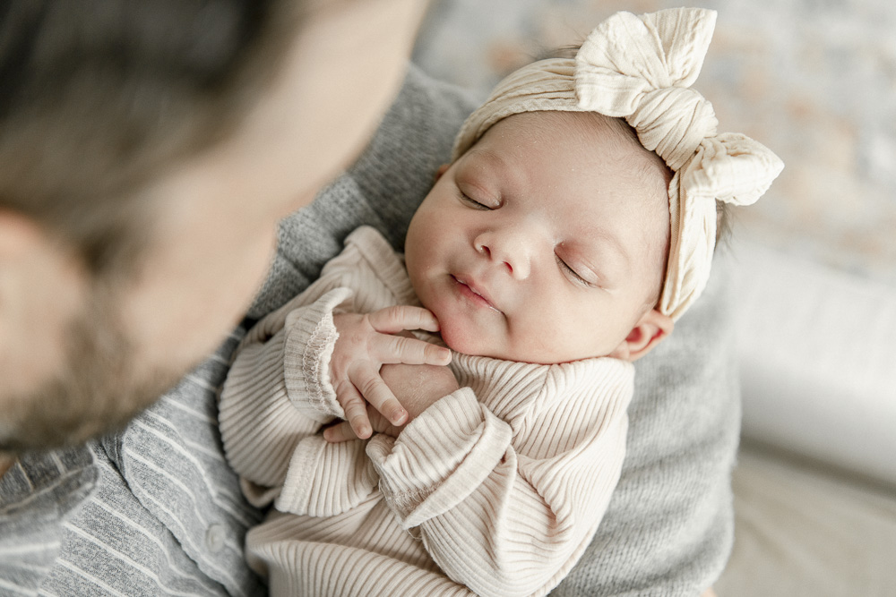 A newborn baby in her father's arms wearing a turban style bow