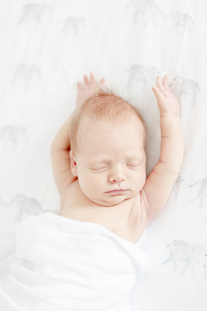 When to book newborn photos: Red haired newborn baby sleeps with arms above her head in her Nashville home
