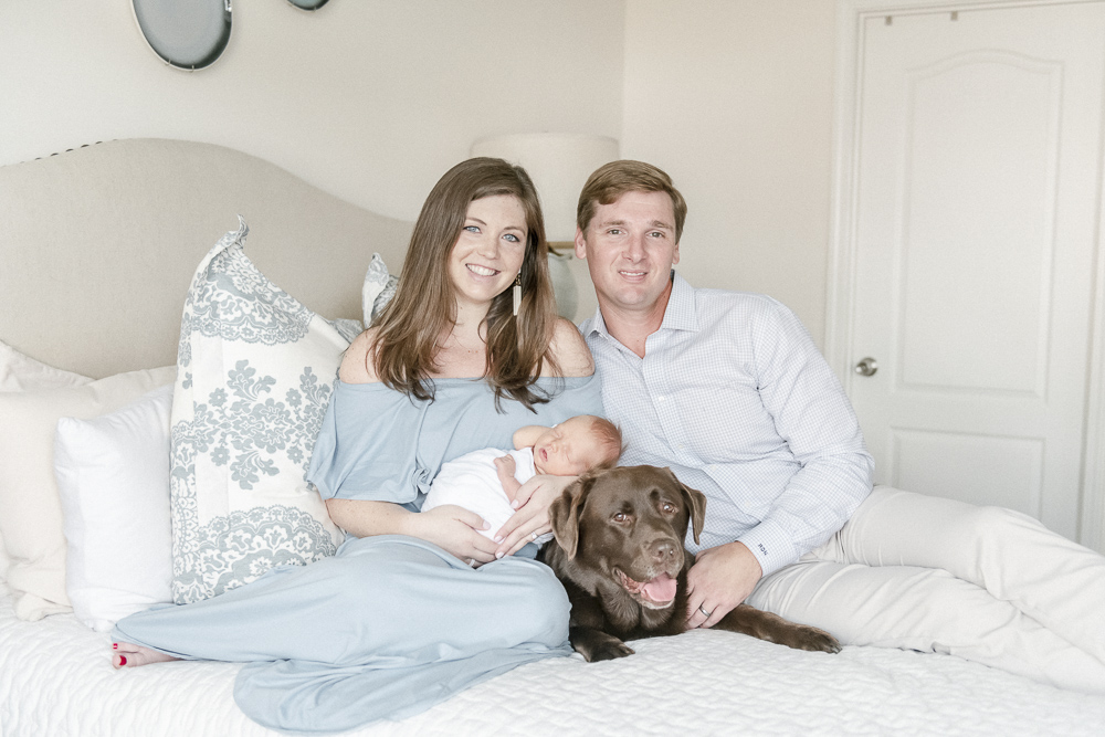 Nashville newborn parents sit on a bed with their baby and chocolate lab