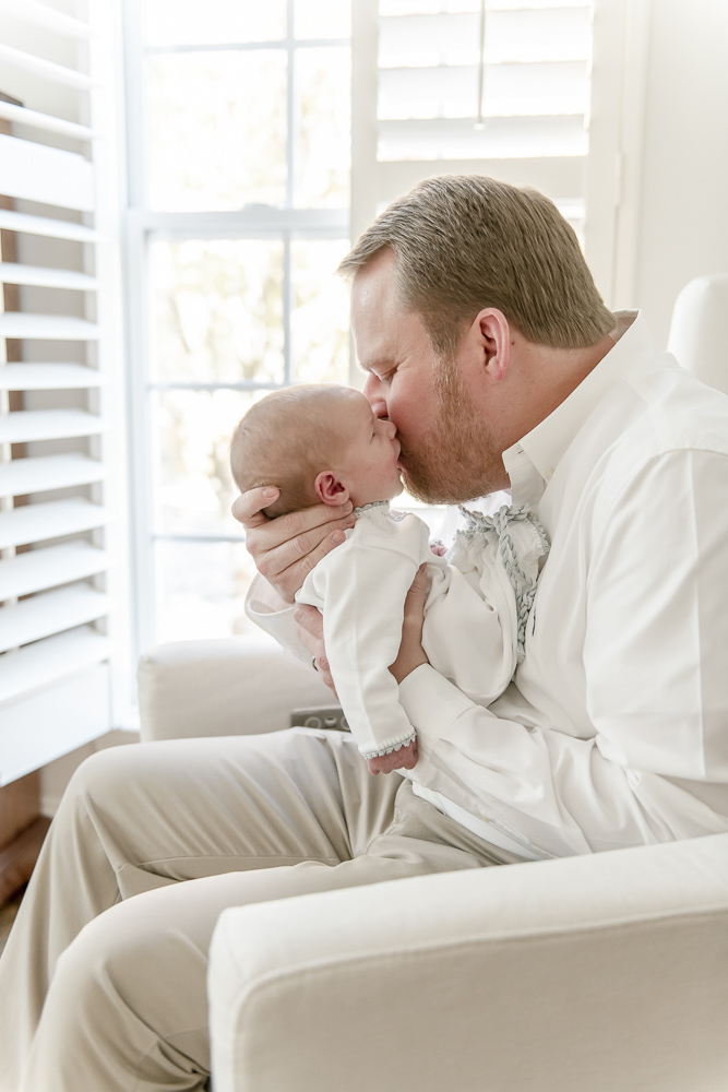 A father kisses his newborn as he sits in a rocking chair in his Nashville home's nursery.