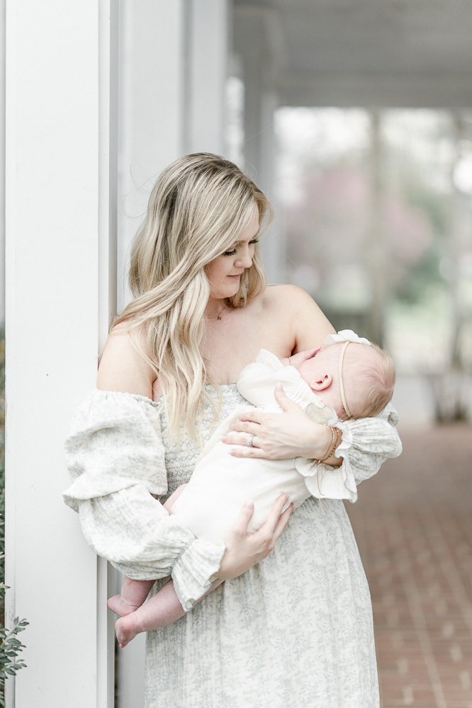 A mother in a white dress stands on a white porch in downtown Franklin TN holding her baby for a mommy and me mini-session