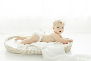 6 month photos of baby girl in a diaper cover lays on her tummy in a Moses basket in Nashville baby photographer Kristie Lloyd's studio