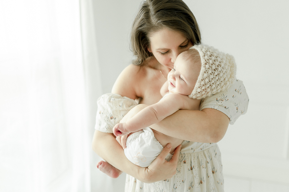 A mother cradles her 6 moth old baby in a white bonnet in Kristie Lloyd's Nashville photography studio