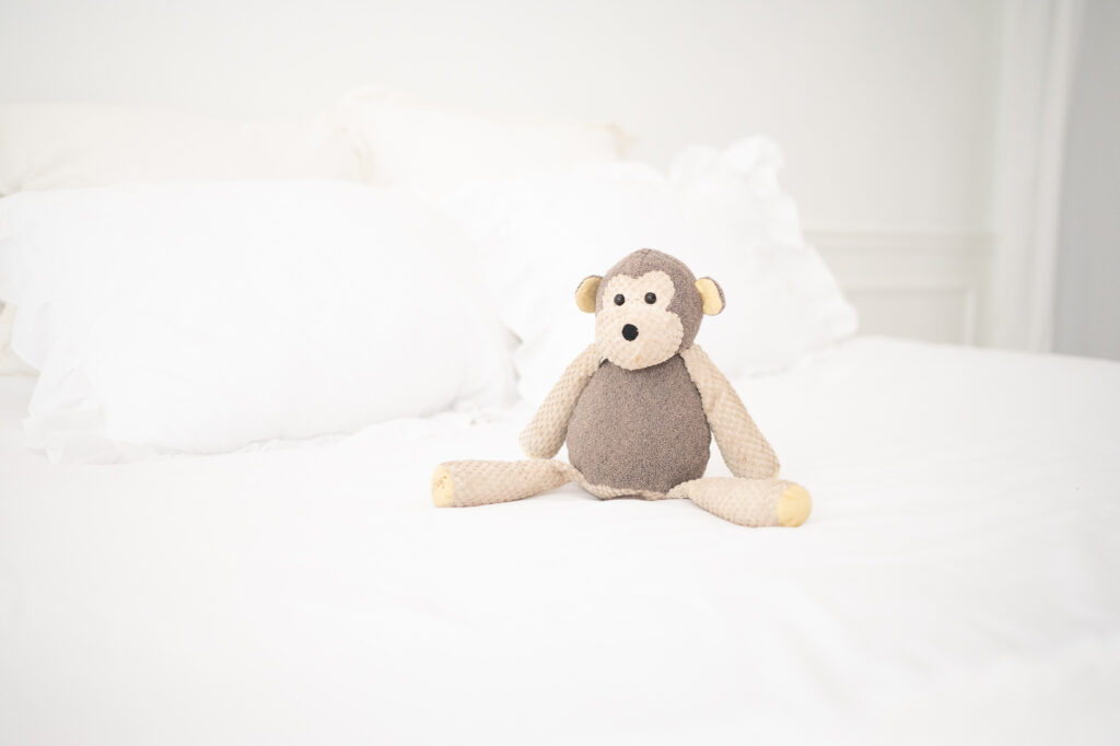 A stuffed monkey sits on a white bed shot at ISO2500