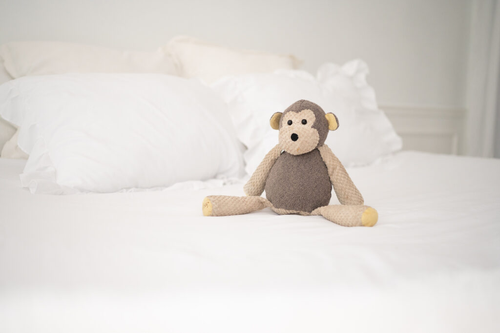 A stuffed monkey sits on a white bed shot at ISO2500