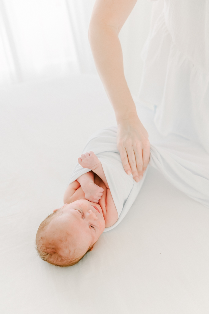 Newborn photographer swaddles a baby with white cloth