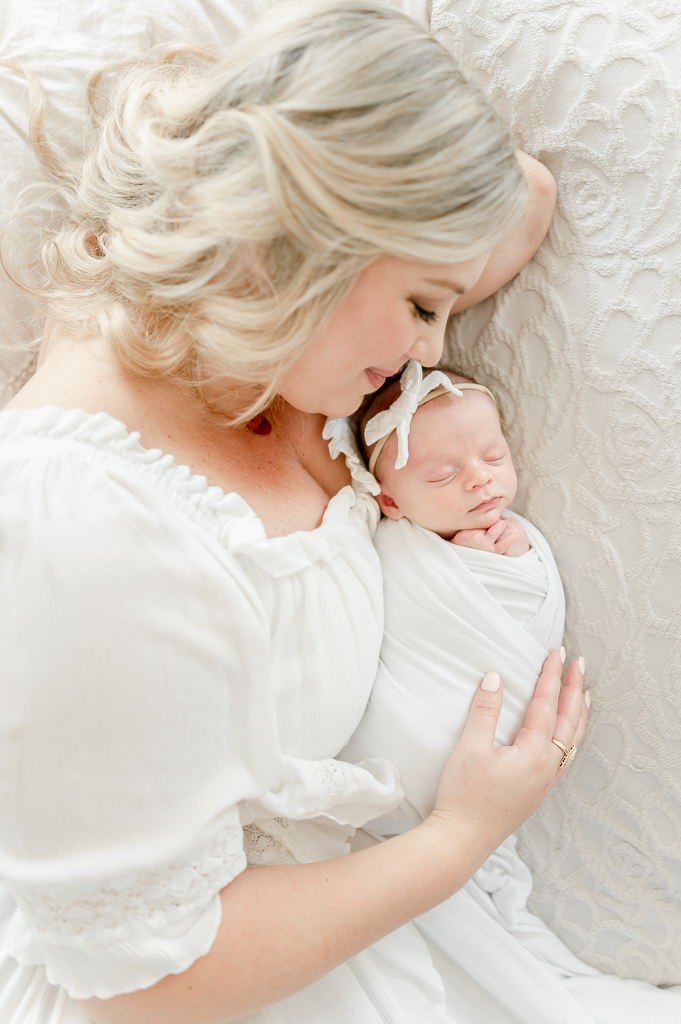 A mother snuggles with her baby swaddled in white  by Brentwood newborn photographer Kristie Lloyd.