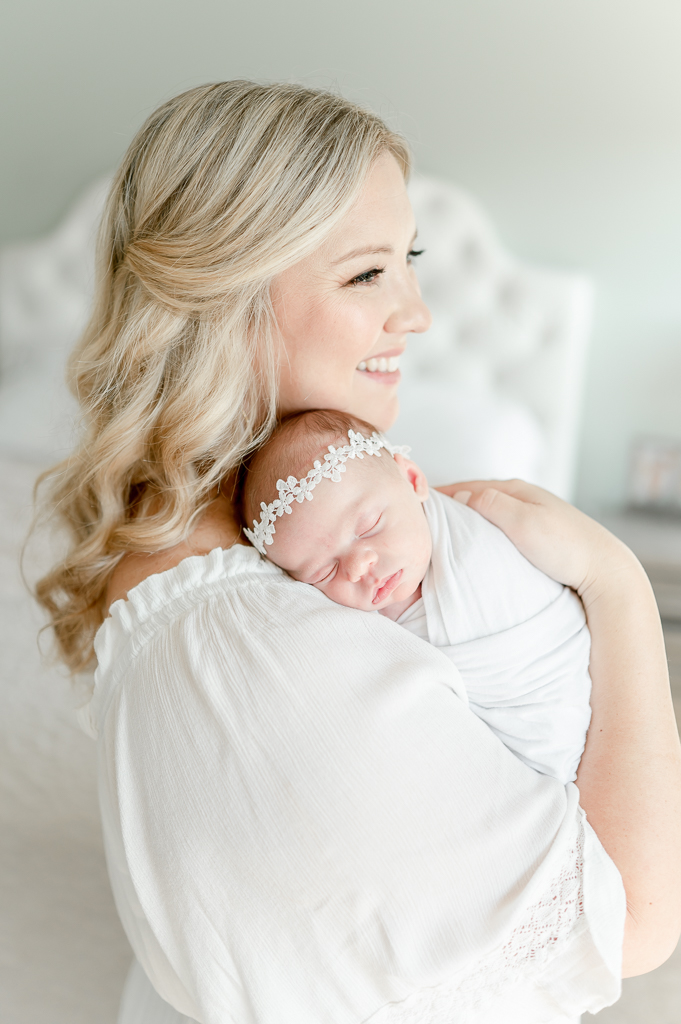 A mother holds her baby and smiles out the window  by Brentwood newborn photographer Kristie Lloyd.
