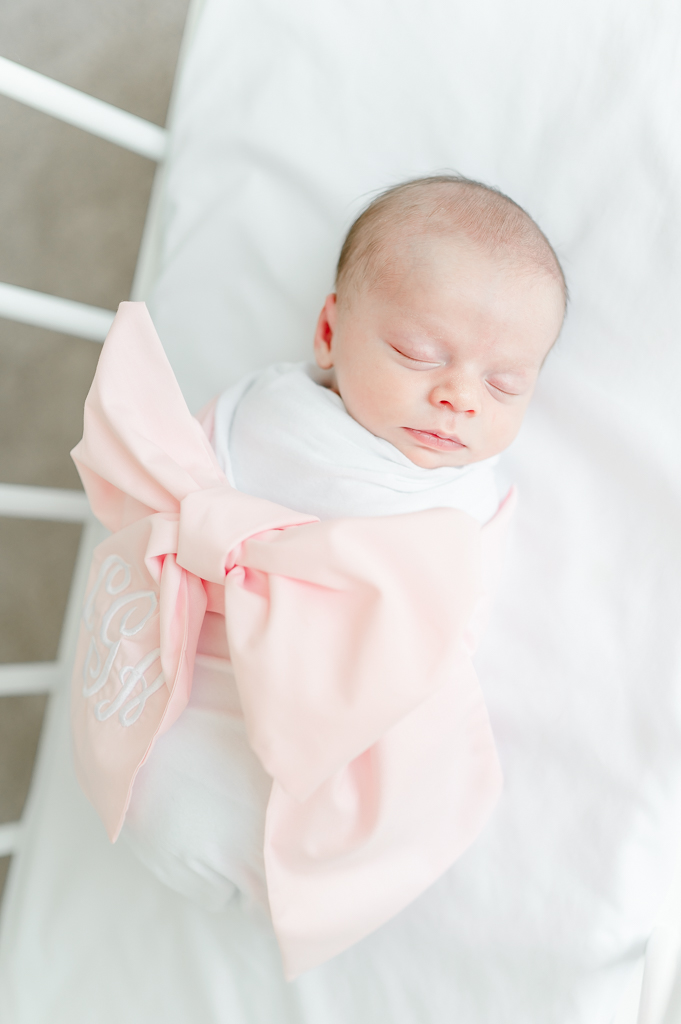 A newborn lays in her crib wrapped in a Beaufort Bonnet swaddle bow  by Brentwood newborn photographer Kristie Lloyd.
