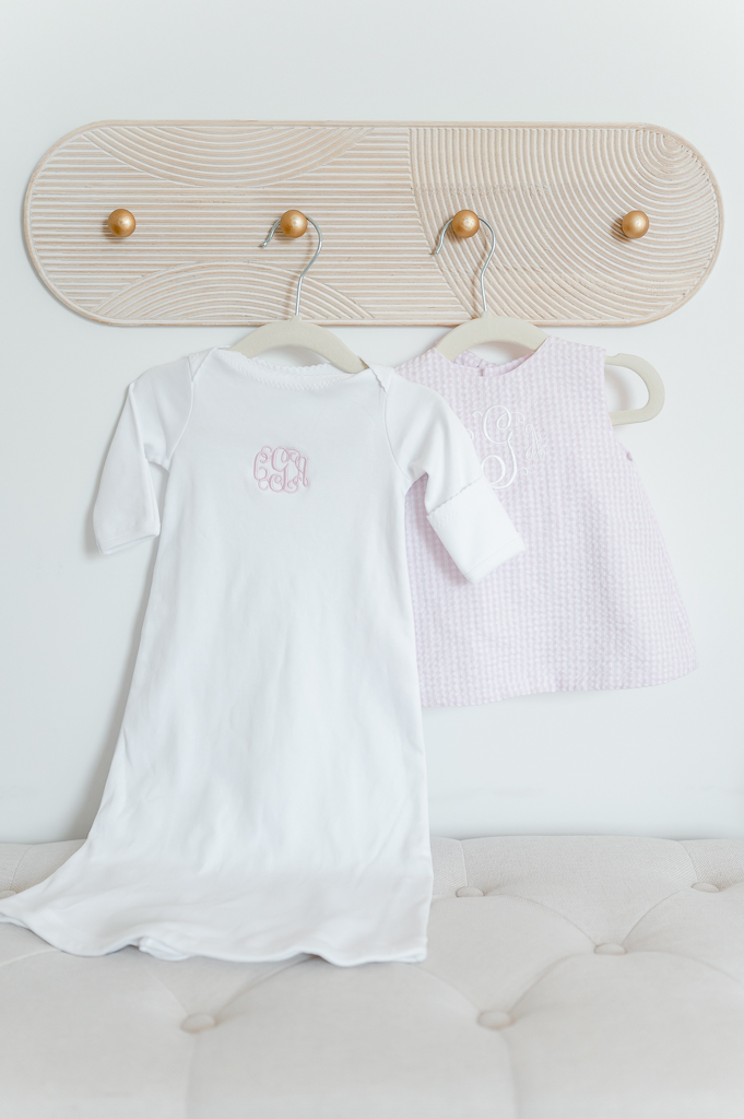 Monogrammed baby gowns hang on a nursery wall