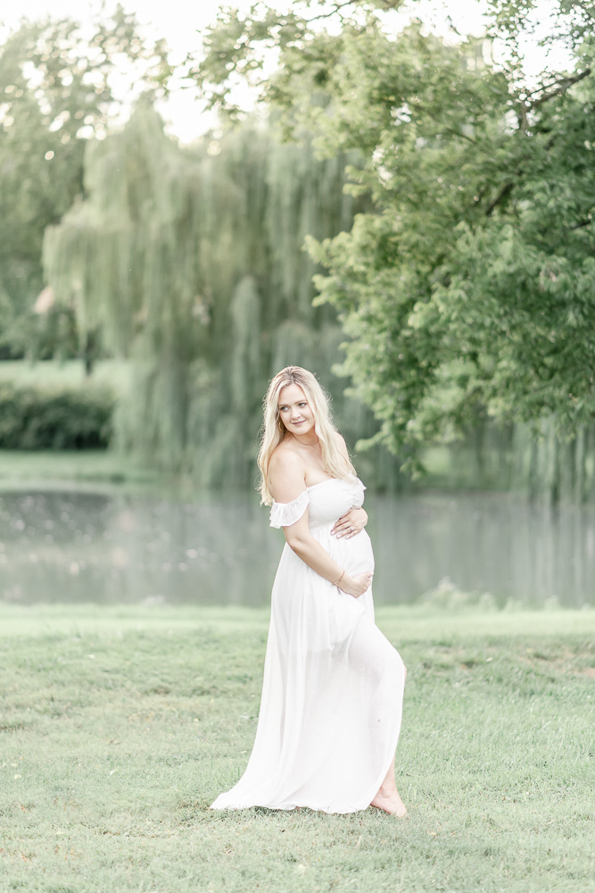 A pregnant woman hugs her abdomen in front of a pond and weeping willow by Franklin TN Maternity photographer Kristie Lloyd.