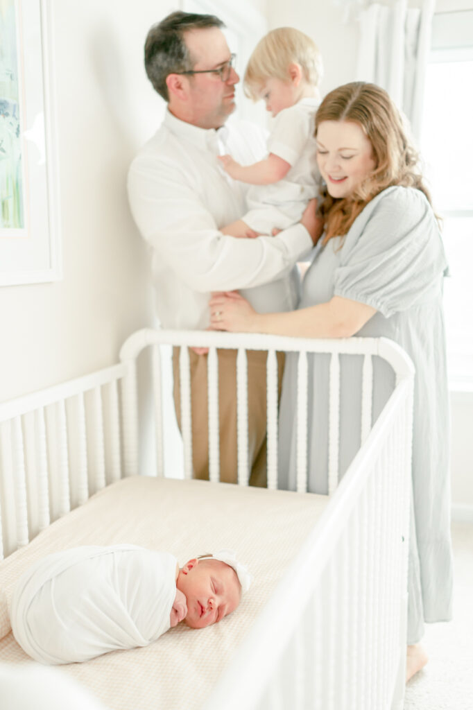 A young family stands over the crib in their Nashville nursery smiling at their newborn baby
