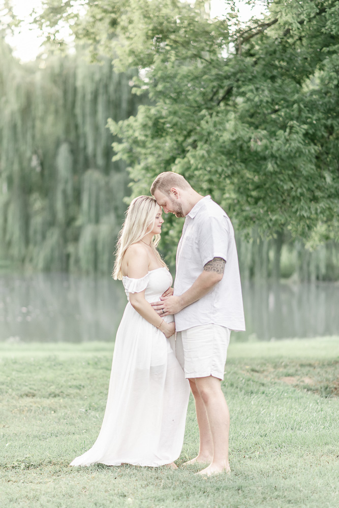 Pregnant couple embrace under a willow tree at sunset