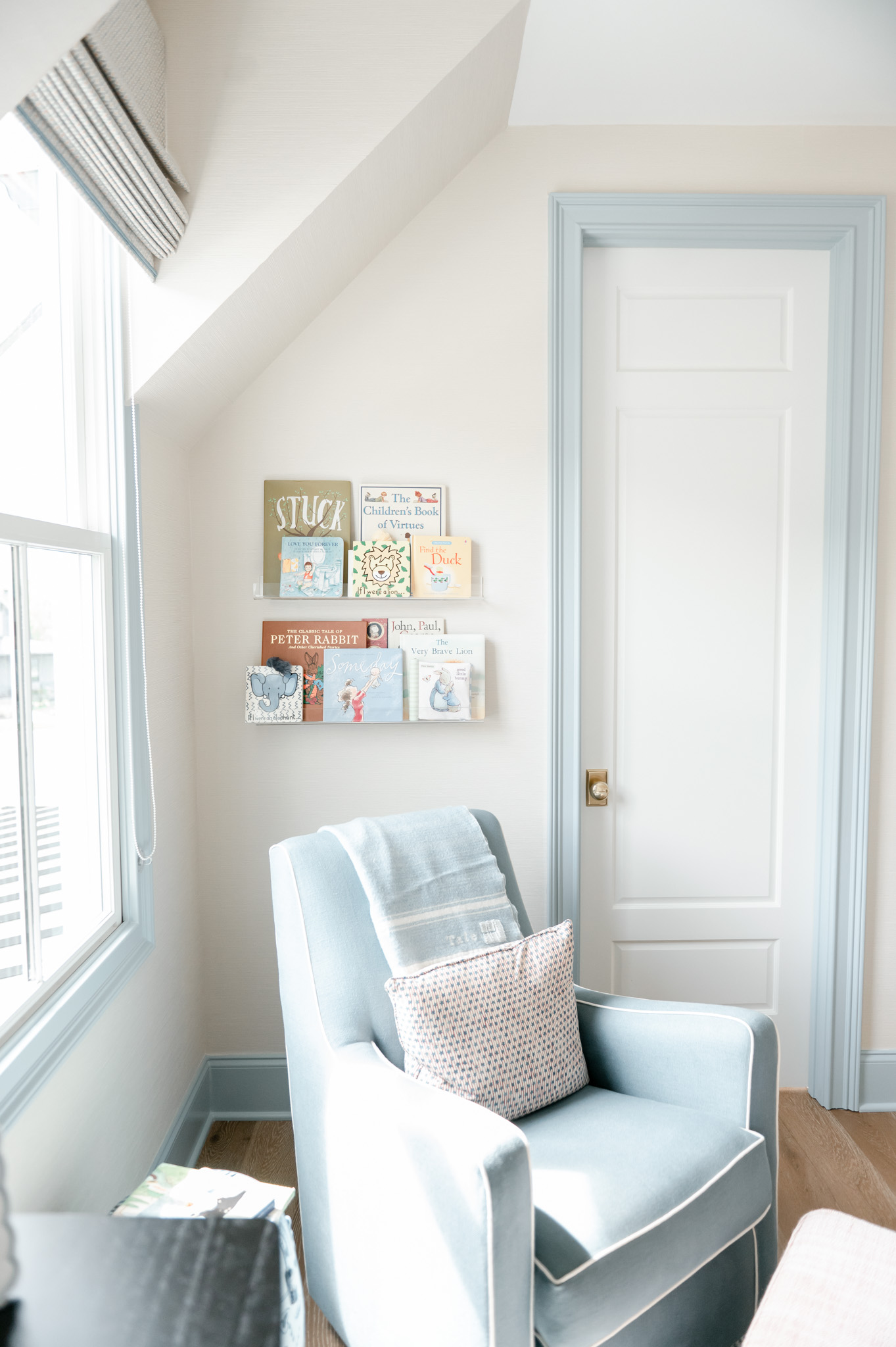 Nursery inspiration : a blue rocking chair with a shelf of children's books hanging on the wall