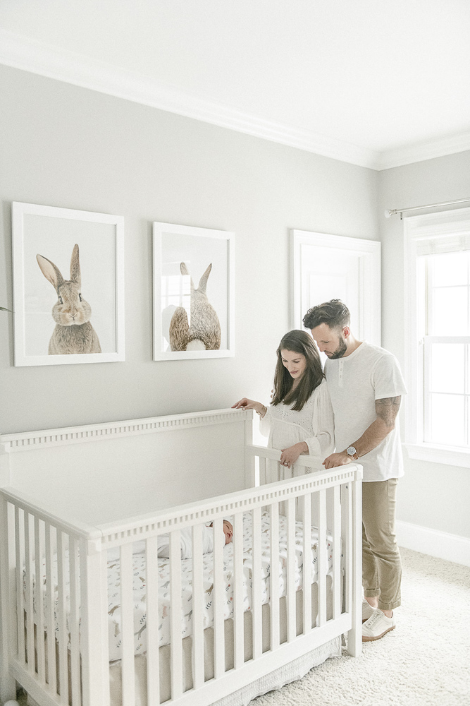 New parents stand over their baby's crib with framed rabbit art above it