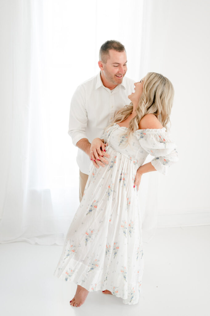 Husbands rests his hand on his wife's pregnant stomach during studio maternity photos with Kristie Lloyd. 