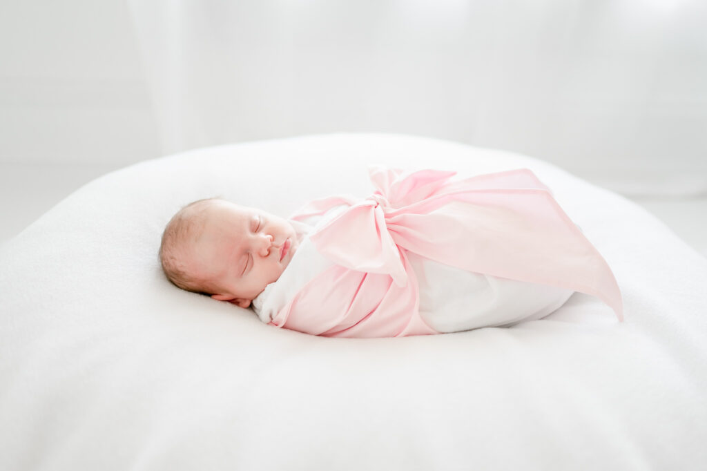 Studio newborn session featuring a baby girl swaddled in a pink beaufort bonnet bow.